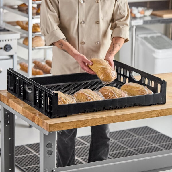 A black plastic bakery bread tray holding several loaves of bread, placed on a wooden table.