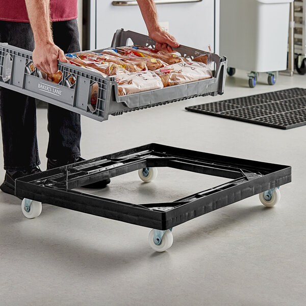 A man using an Orbis Bakery Tray Dolly to move a crate of food.