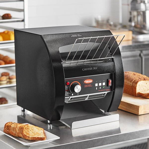 A black Hatco conveyor toaster on a counter with toasted bread on a metal rack.