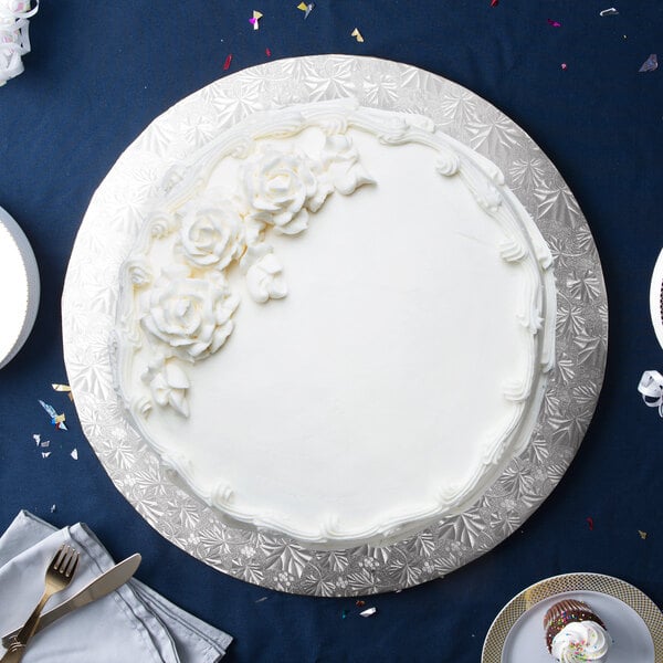 A white cake with white frosting and flowers on a silver Enjay round cake drum on a table.