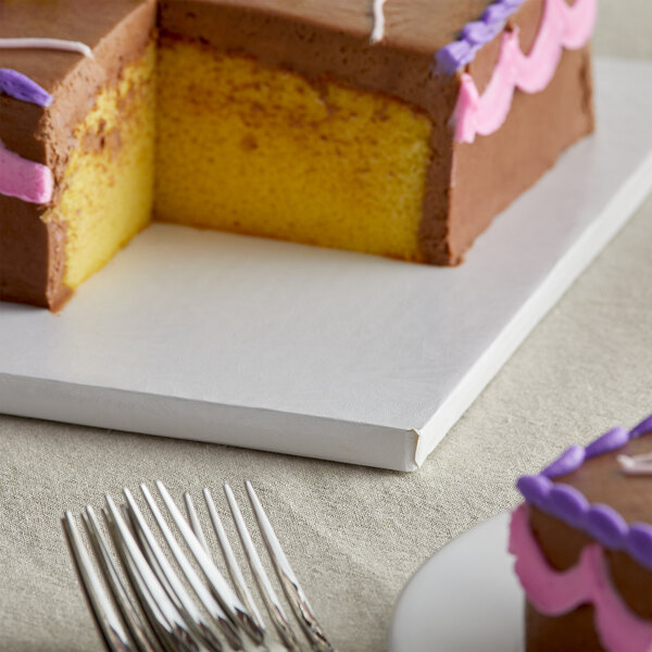 A white square cake drum with a slice of cake with frosting on it.