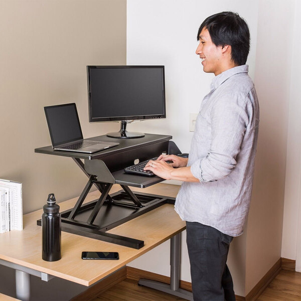 A man using a Luxor black standing desk with a laptop.