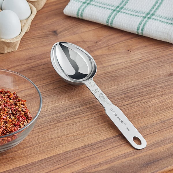 A silver Vollrath stainless steel measuring scoop on a wood table.