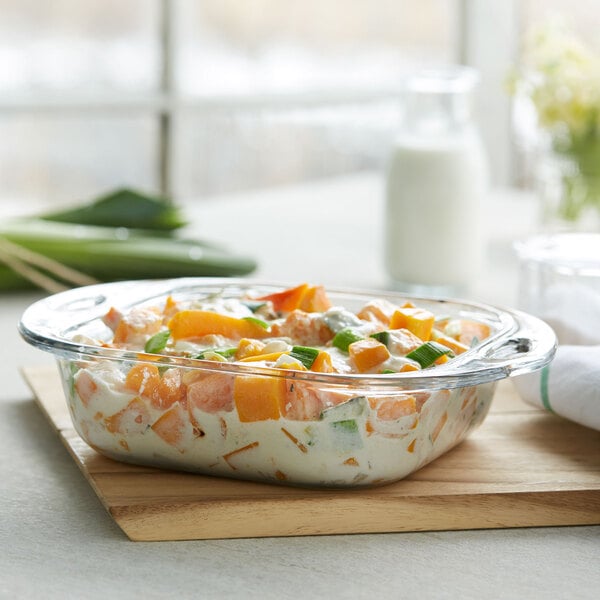 An Anchor Hocking clear glass square cake dish filled with food on a cutting board.