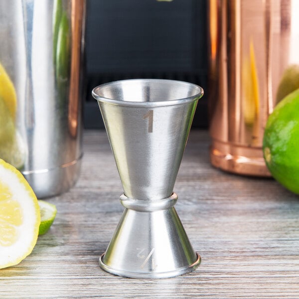 An American Metalcraft stainless steel Japanese style jigger on a table with a lime and lemon.