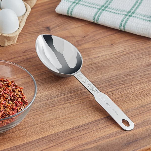 A silver Vollrath stainless steel measuring scoop on a wooden surface.