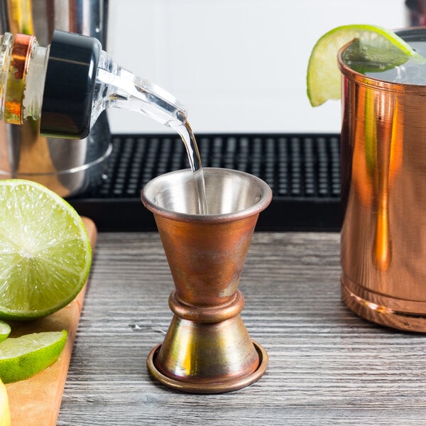 An American Metalcraft copper Japanese style jigger on a wood surface with lime juice and a lime wedge.