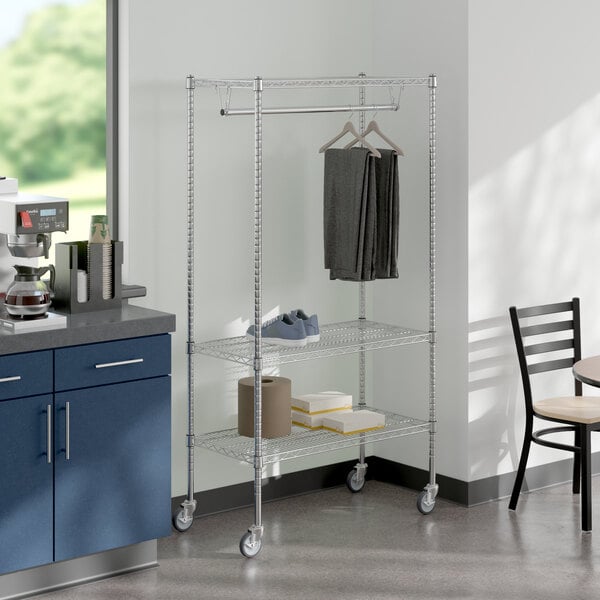 A room with a kitchen and a table and a Regency Chrome Mobile Garment Rack with clothes.