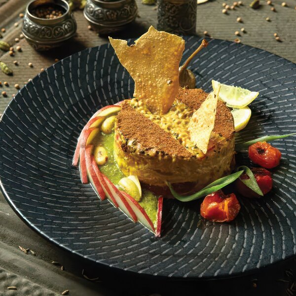 A Luzerne Urban by Oneida black porcelain coupe plate with food on it.