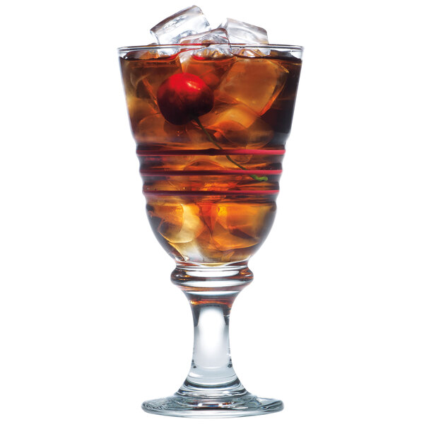 A glass of brown liquid with ice and a cherry.