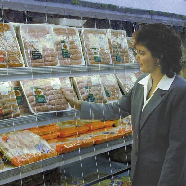 A woman looks at a display cooler of meats through a Curtron strip curtain.