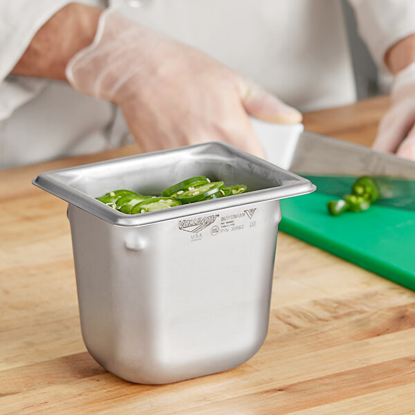 A hand using a Vollrath stainless steel container to hold sliced jalapenos.