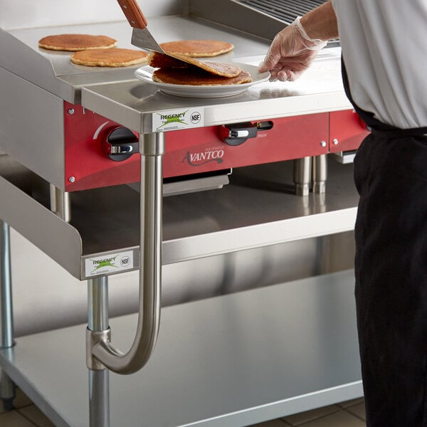 A person using a Regency stainless steel work surface to cook pancakes.