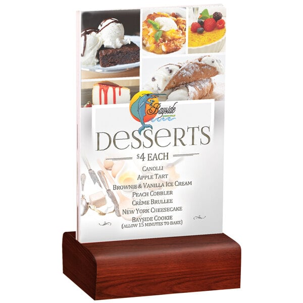 A clear acrylic Menu Solutions table tent with a mahogany wood base on a table with a dessert display.