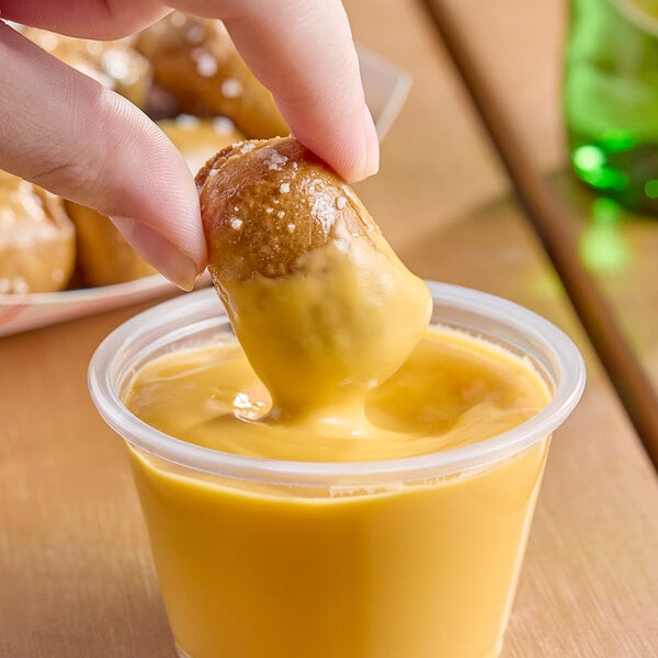 A person dipping a small pretzel into a cup of Gehl's jalapeno cheese sauce.