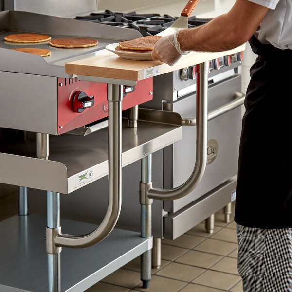 A man using a Regency 10" x 30" wooden cutting board to cook on a counter.