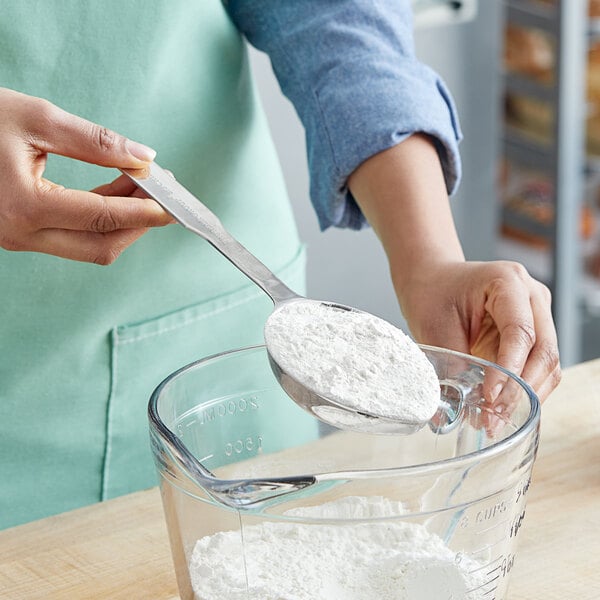 A person using a Thunder Group stainless steel measuring scoop to add flour to a bowl.