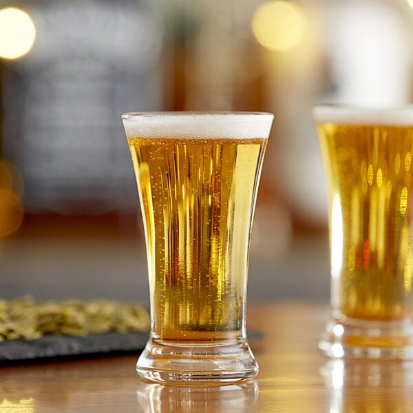 Two Libbey flare shooter glasses filled with beer on a table.