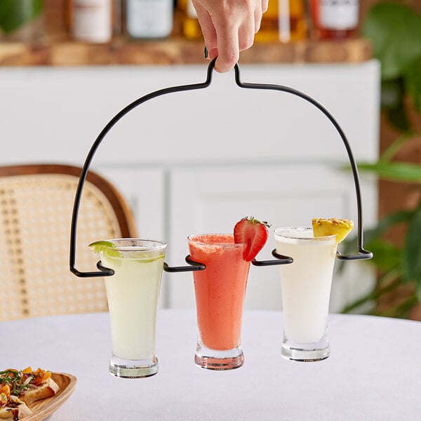 A hand holding a Vollrath metal swinger with three glasses of different drinks.