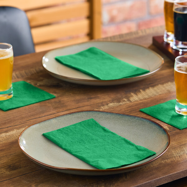 Two beige plates with green napkins are set on a wooden table, accompanied by glasses of beer and additional green napkins used as coasters.