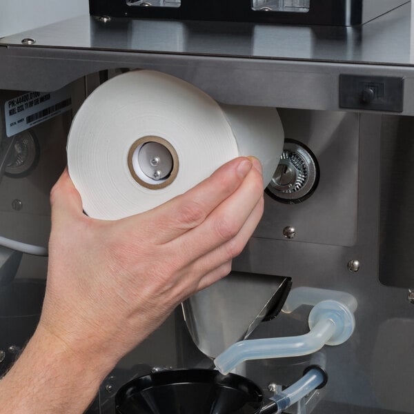 A hand holds a roll of Bunn paper filters in front of a black coffee filter container.