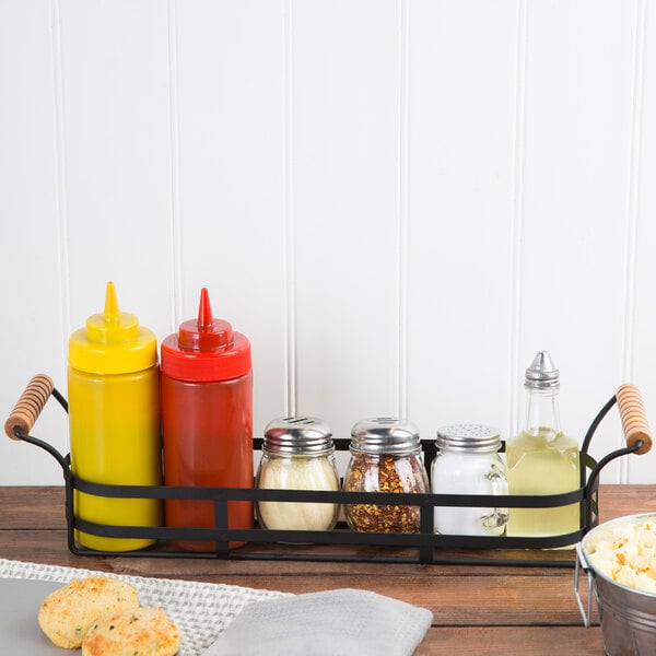 A Tablecraft black metal condiment caddy with red and yellow condiment containers and a glass jar with a metal lid.