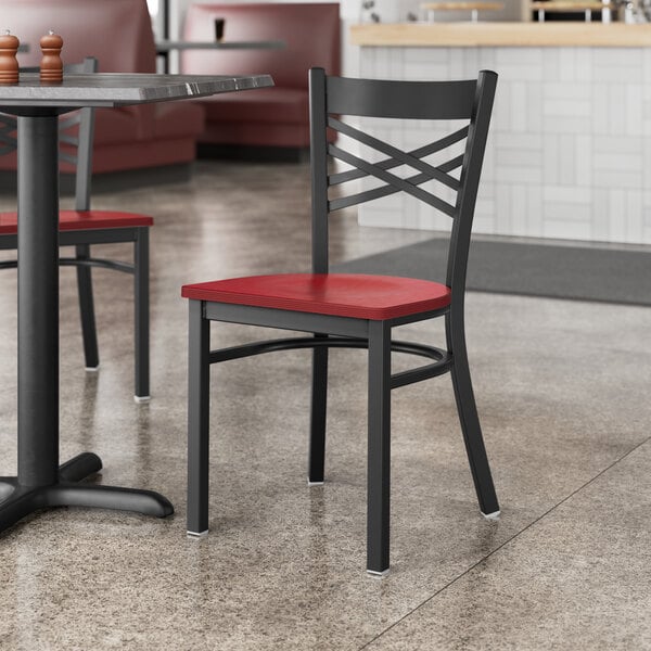 A Lancaster Table & Seating black cross back chair with a mahogany wood seat on a table in a restaurant.