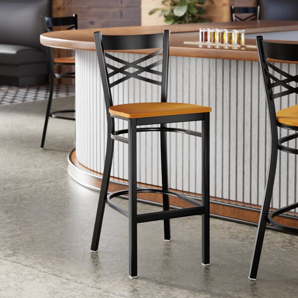 A black metal bar stool with a cross back design and a cherry wood seat.