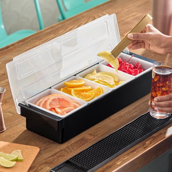 A four-compartment condiment bar containing sliced fruits and cherries, used for drink garnishes.
