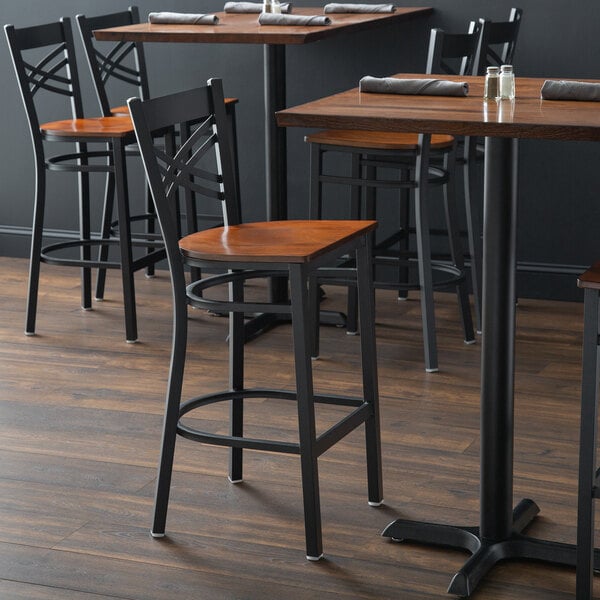 A black metal bar stool with a cross back design and an antique walnut wood seat.