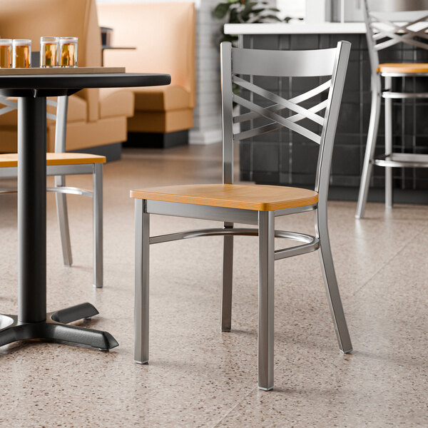 A metal cross back chair with a natural wood seat, designed for commercial dining settings.