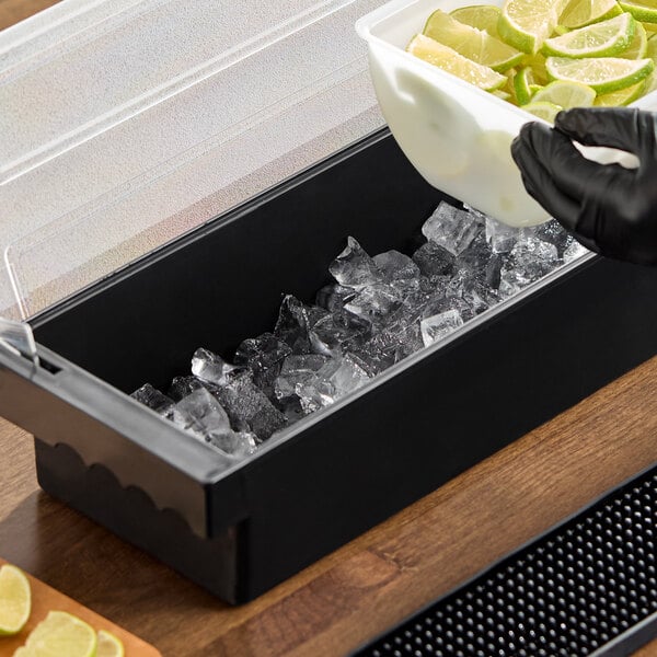A black 6-compartment condiment bar with a clear lid, partially filled with ice and being stocked with lime wedges.