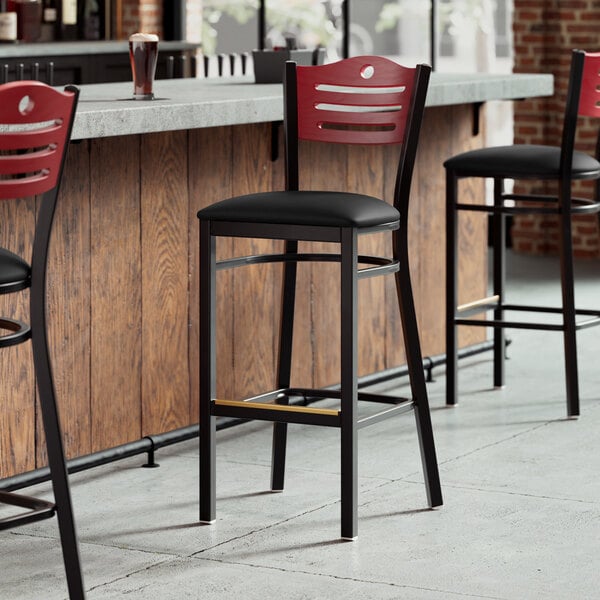 A Lancaster Table & Seating black restaurant bar stool with a black vinyl seat and mahogany wood back.