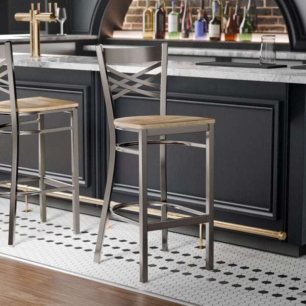 A metal bar stool with a cross back design and a driftwood-colored wooden seat.