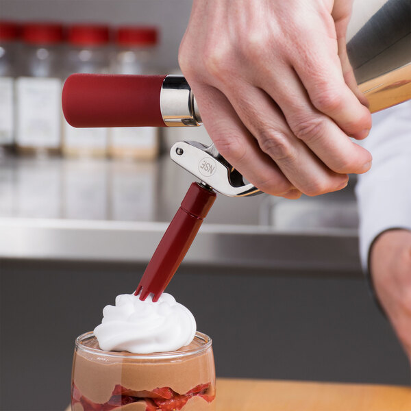 A person using an iSi red charger holder to put whipped cream on a dessert.