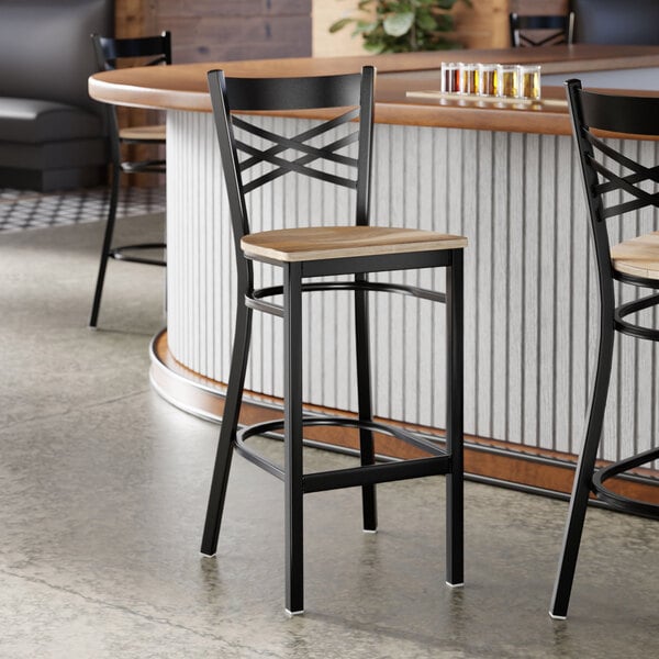 A black metal bar stool with a cross back design and a driftwood-colored wooden seat.