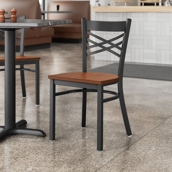 A Lancaster Table & Seating black cross back chair with an antique walnut wood seat at a table in a restaurant.