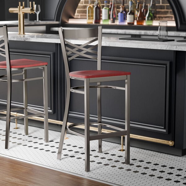 A metal bar stool with a cross back design and a mahogany wood seat, placed at a bar counter.