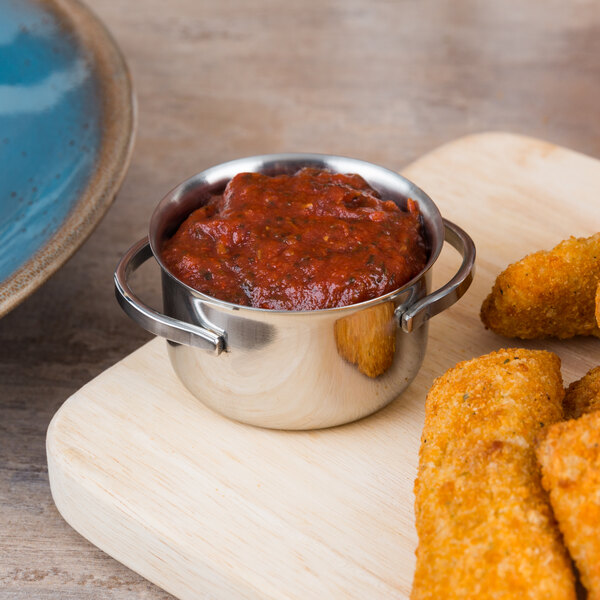 A mini stainless steel pot of red sauce next to fried chicken sticks.