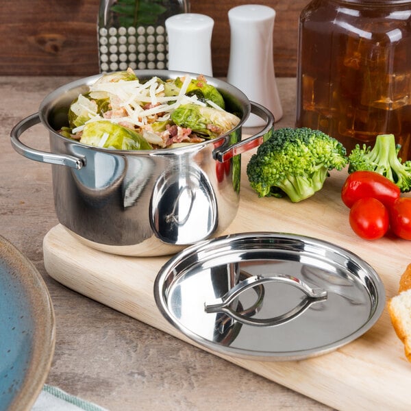 An American Metalcraft stainless steel pot with a lid filled with food on a table with a head of broccoli.