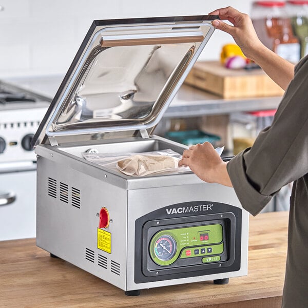 A person using an ARY VacMaster chamber vacuum packaging machine to seal a bag of food on a counter.