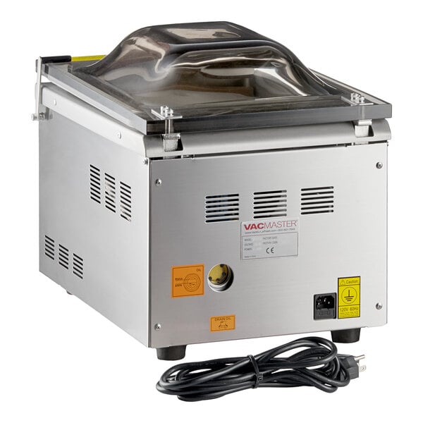 A stainless steel chamber vacuum packaging machine with a clear domed lid and a power cord.