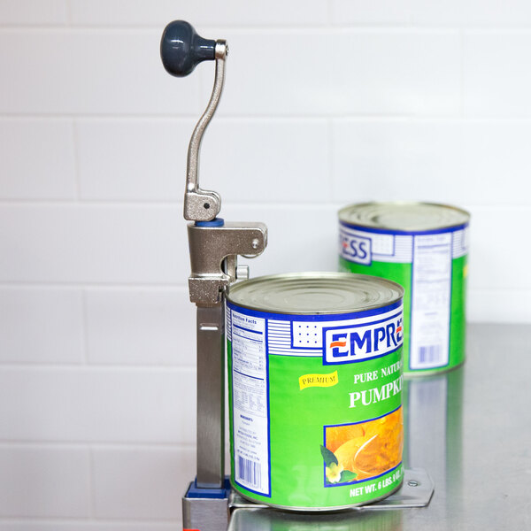 An Edlund Standard Duty Manual Can Opener with a can of food on a metal stand.