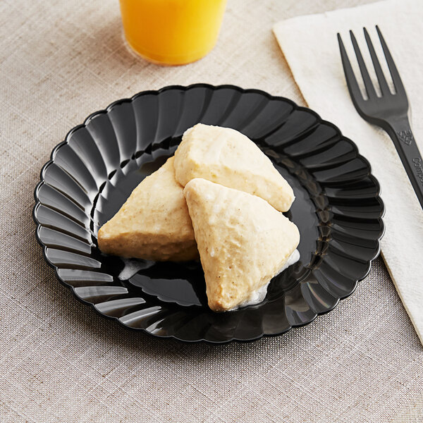 A black WNA Comet Classicware plastic plate with food on it next to a fork and knife.