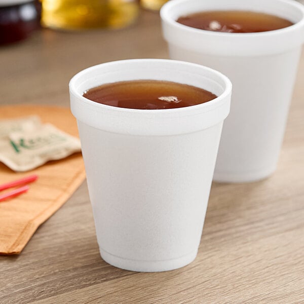 Two Dart white foam cups filled with brown liquid on a table.
