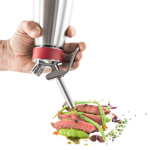 A hand using a stainless steel iSi decorating tip to pipe food into a silver cup.