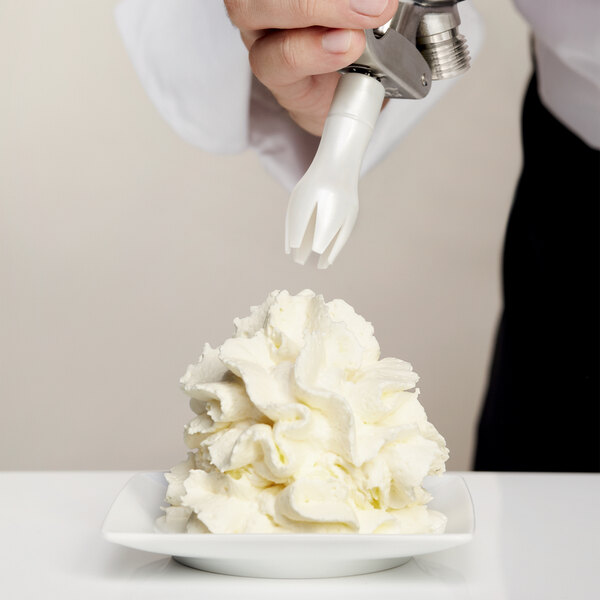 A hand using an iSi tulip decorator tip to pipe white frosting on a plate.