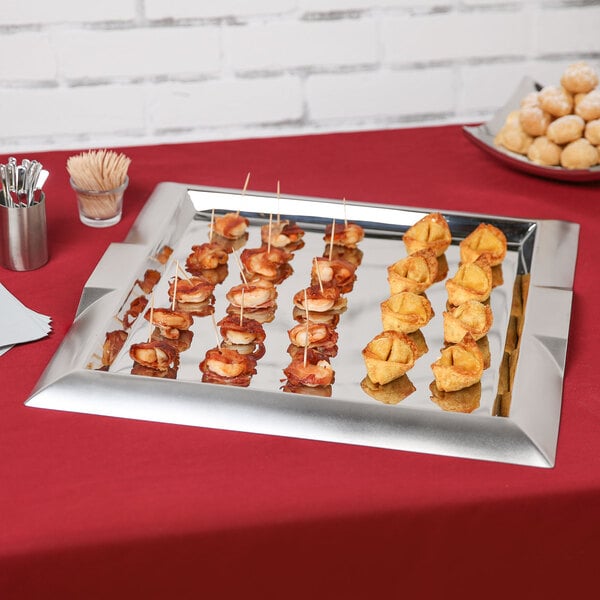 A Vollrath stainless steel square serving tray with appetizers on a table.