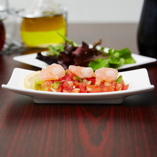 An Arcoroc rectangular porcelain plate with shrimp and vegetables on a table.