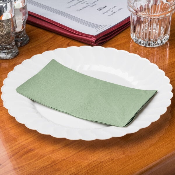 A Hoffmaster soft sage green paper dinner napkin on a white plate.